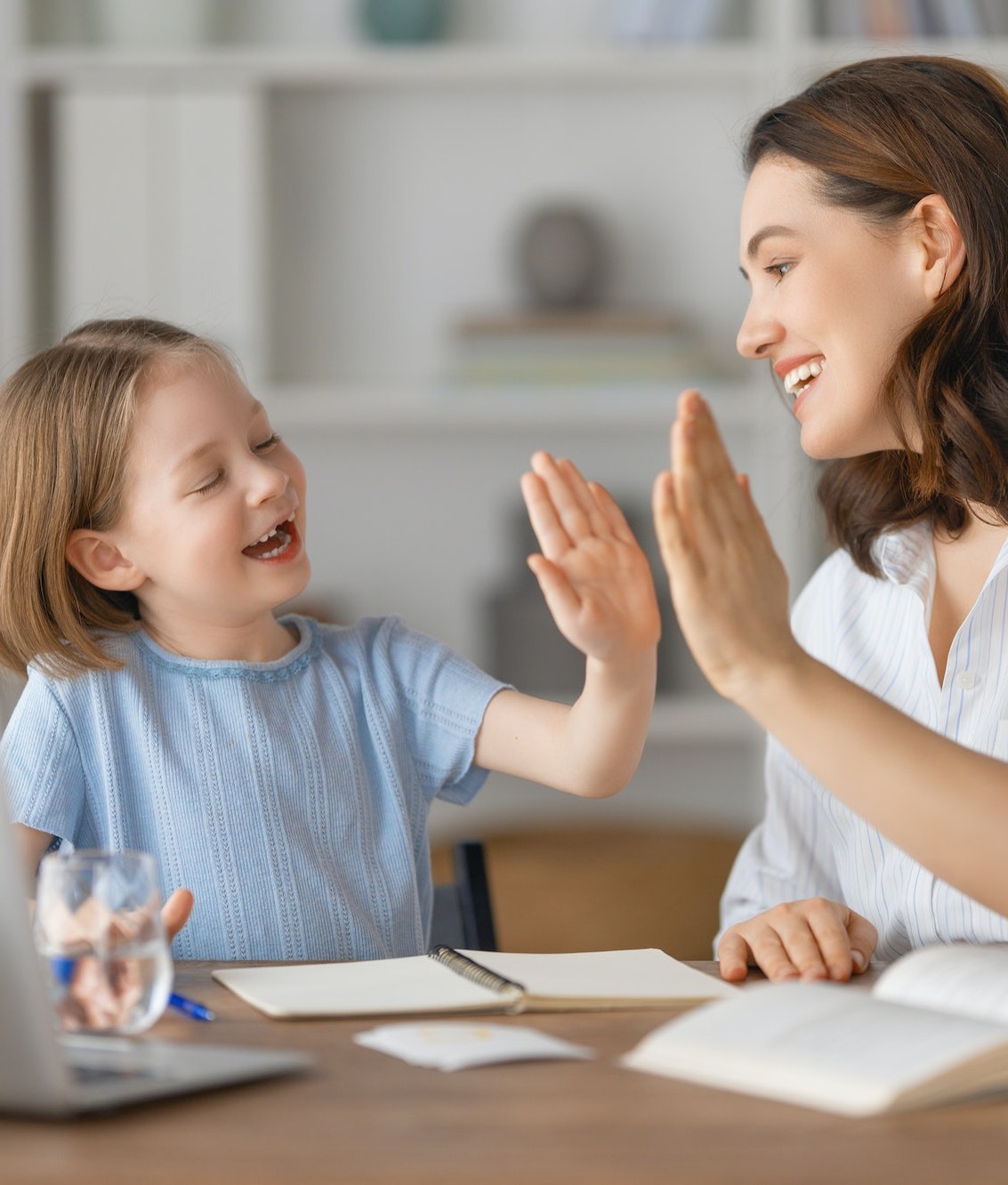 A mother and daughter sharing a high five at their kitchen table